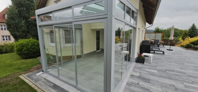 Une véranda moderne vitrée, dotée d'une structure en aluminium, construite sur la vaste terrasse d'une maison individuelle.