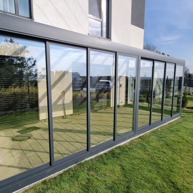 Une véranda moderne à la structure en aluminium et aux grandes baies vitrées, attenante à une maison individuelle dotée d'une pelouse verdoyante.