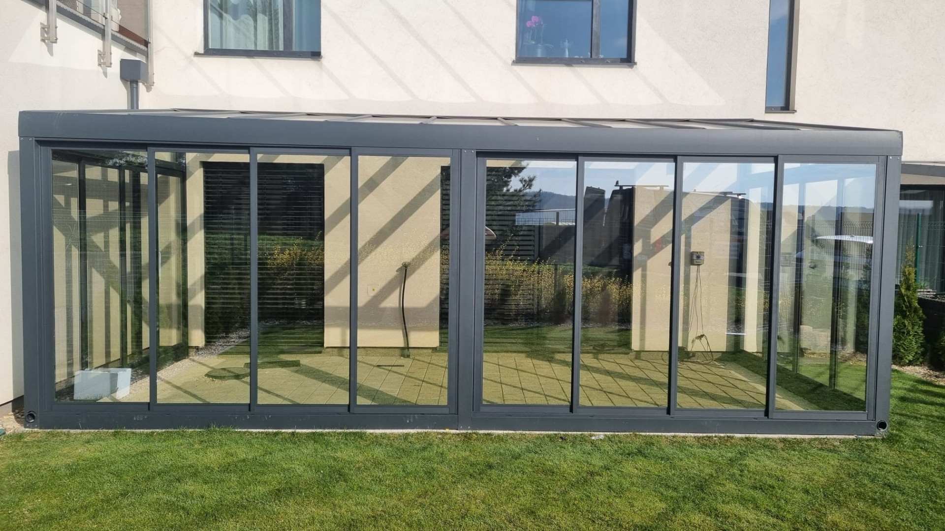Une véranda moderne en aluminium et verre attenante à une maison individuelle, avec vue sur la pelouse.