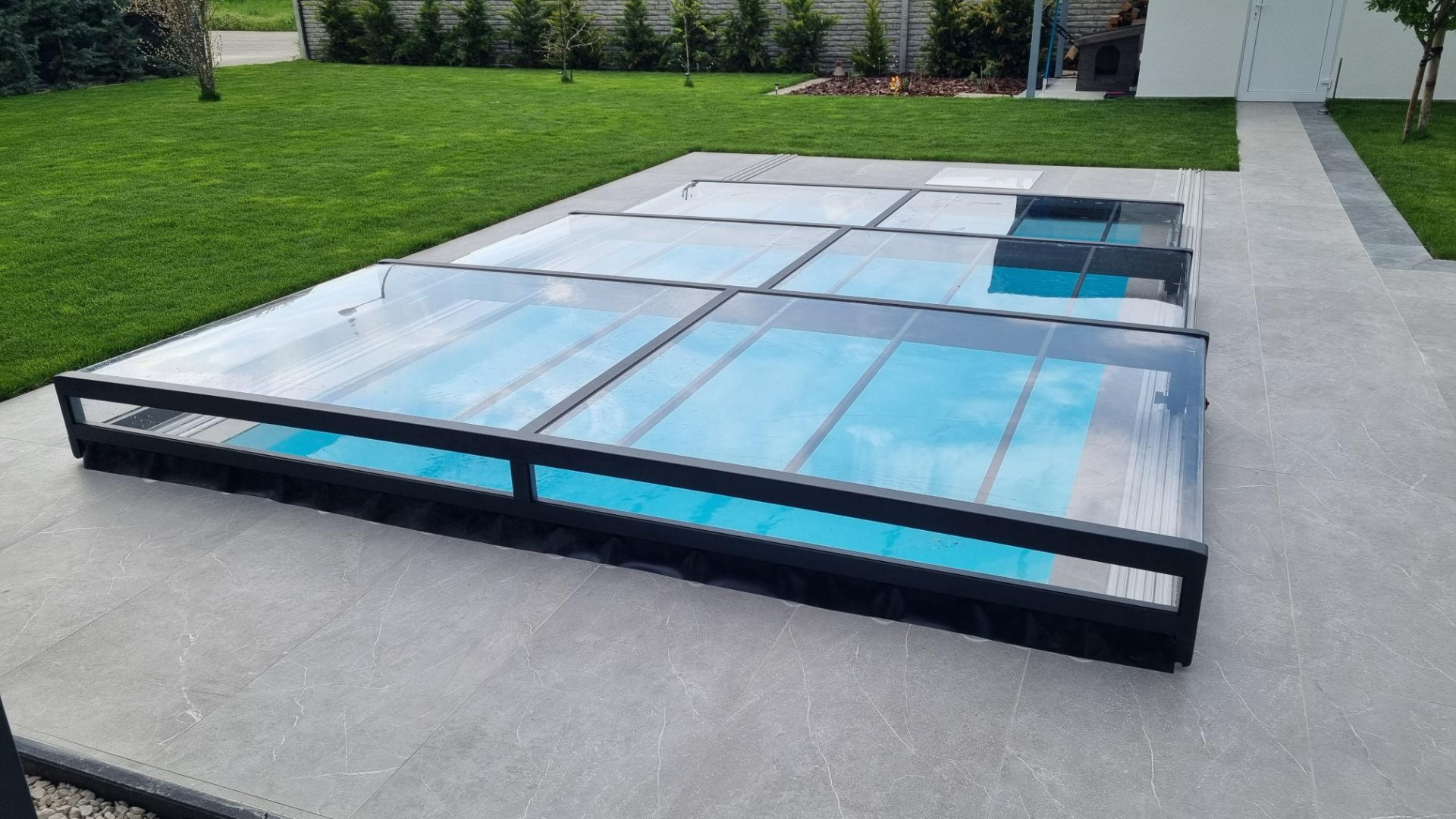 Une couverture de piscine moderne et basse en aluminium, avec un cadre anthracite et du verre transparent, dans le jardin
