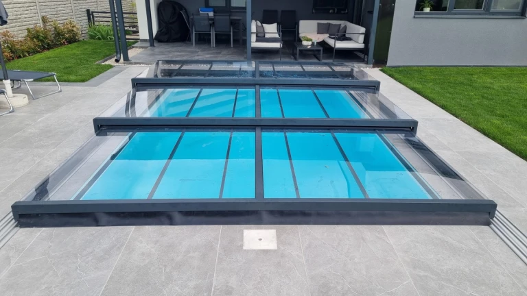 Une couverture de piscine moderne et basse en aluminium, dotée d'un panneau transparent, installée sur la terrasse d'une maison individuelle