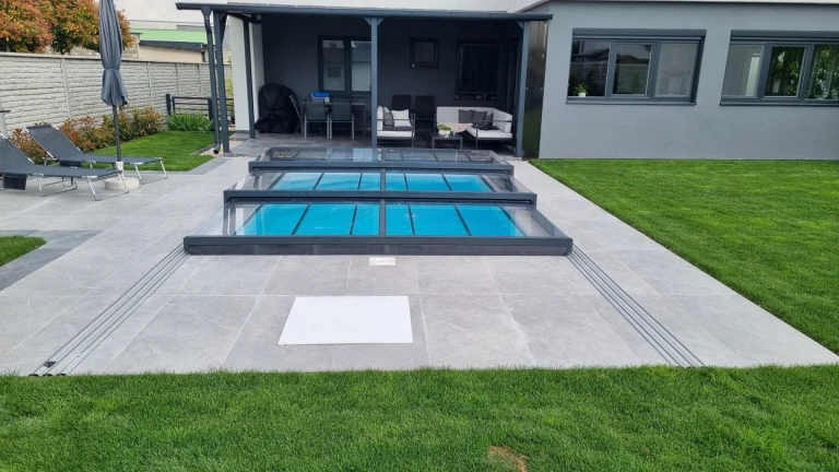 Une couverture de piscine moderne et basse en aluminium, de couleur anthracite, installée sur la terrasse d'une maison individuelle