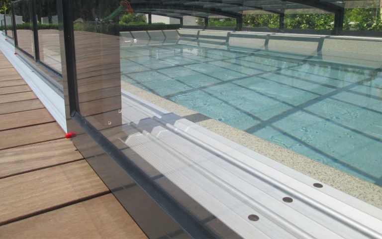Vue détaillée du rail et de la structure de la petite verrière au-dessus de la piscine, sur la terrasse en bois.