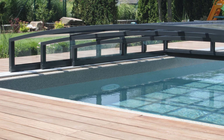 Vue détaillée de la couverture basse en aluminium de la piscine, avec ses rails, sur une terrasse en bois