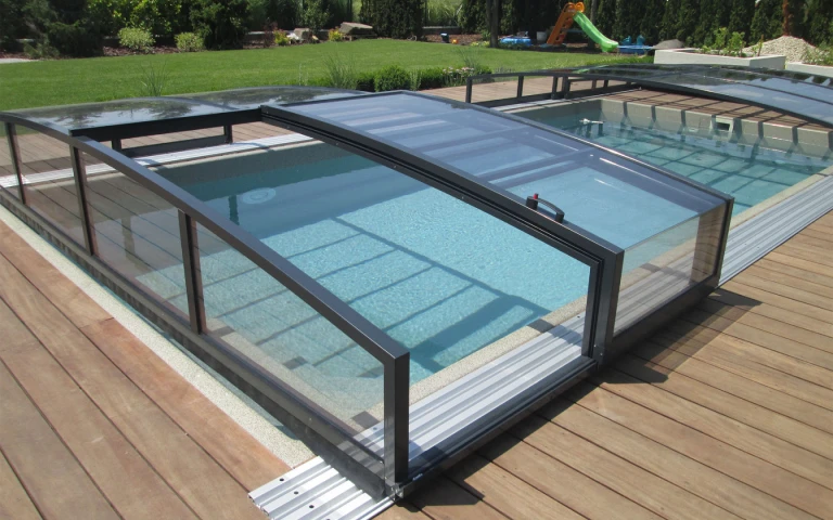 Une abri de piscine moderne, bas et de couleur anthracite, installé sur une terrasse en bois dans le jardin