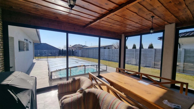 Vue depuis l'intérieur de la terrasse vitrée au plafond en bois sur le jardin avec piscine