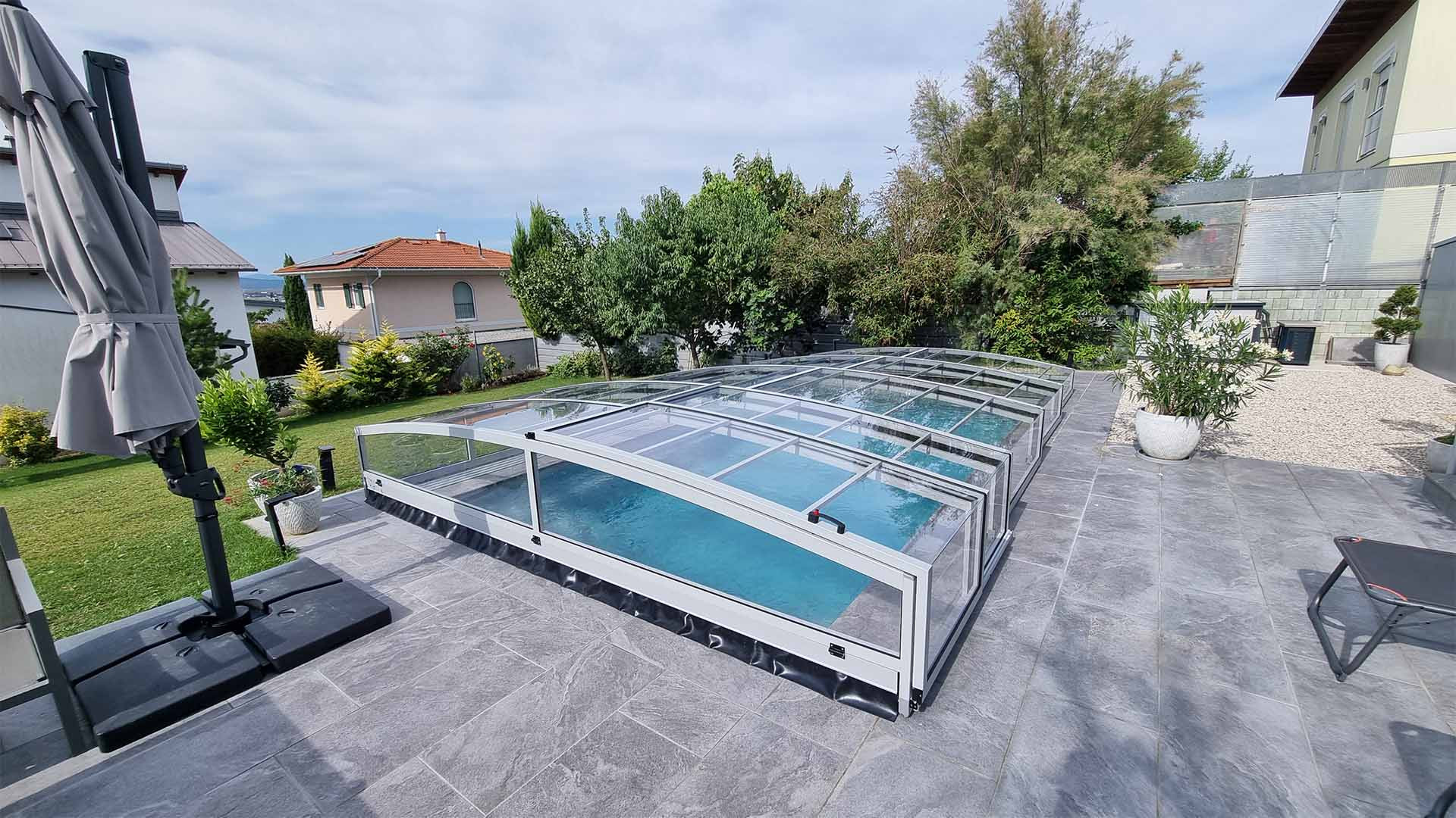 Abri de piscine PREMIER moderne et bas en aluminium, installé sur la terrasse pavée du jardin d'une maison individuelle