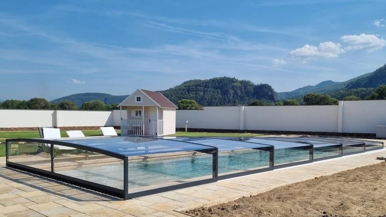 Une verrière moderne et basse surplombant la piscine dans le jardin, avec vue sur les montagnes et un petit abri de jardin.