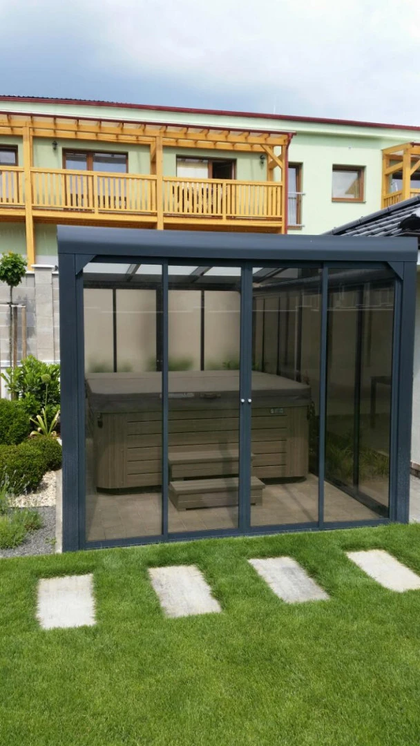 Un abri vitré moderne avec un jacuzzi, situé dans le jardin d'une maison individuelle.