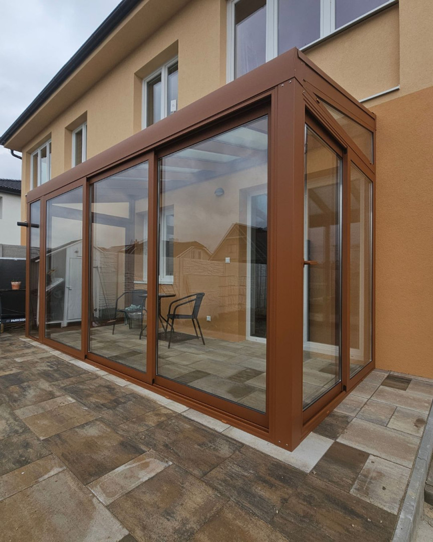 Une véranda moderne à la structure vitrée, dotée d'un cadre marron, attenante à une maison individuelle.