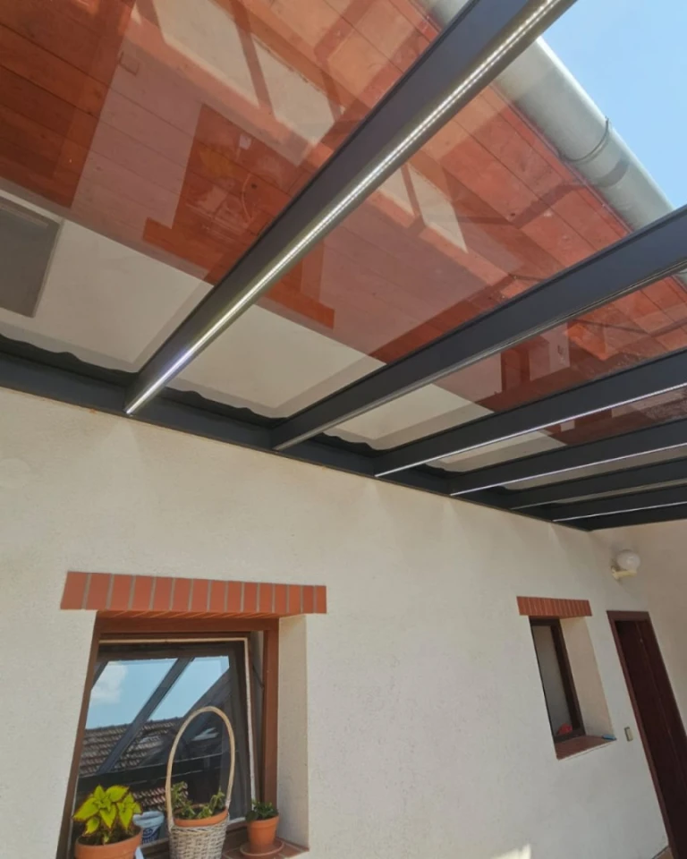 Vue détaillée de la toiture d'une pergola en aluminium dotée d'un éclairage LED intégré, fixée à la façade de la maison.