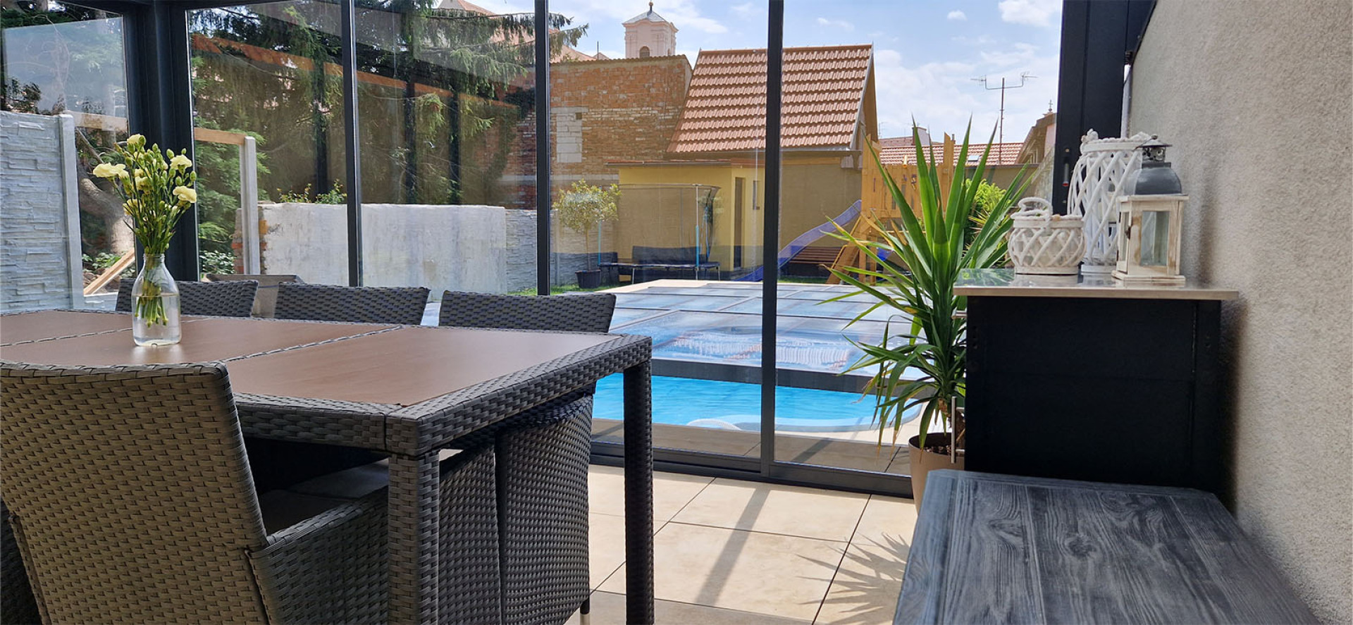 Vue depuis l'intérieur de la véranda, avec du mobilier de jardin, donnant sur la terrasse et la piscine