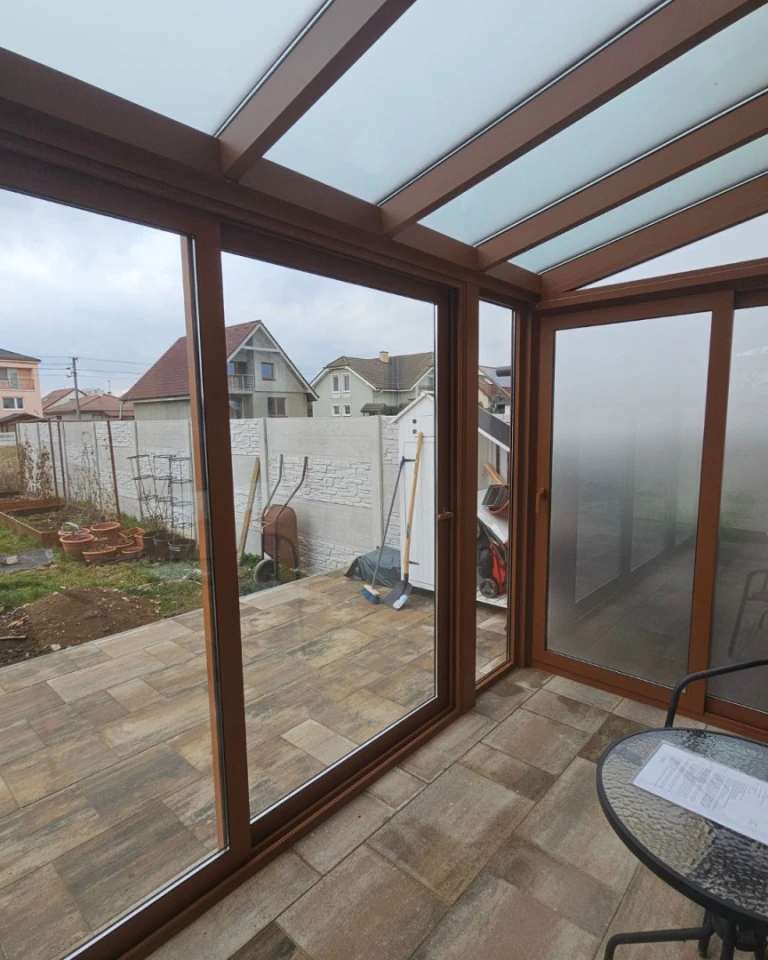 Vue depuis l'intérieur d'un abri vitré à la structure marron sur la cour et les maisons environnantes