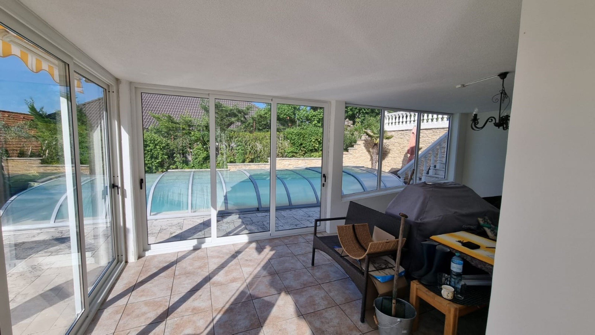 Une terrasse vitrée aux cadres blancs, avec vue sur la piscine dans le jardin