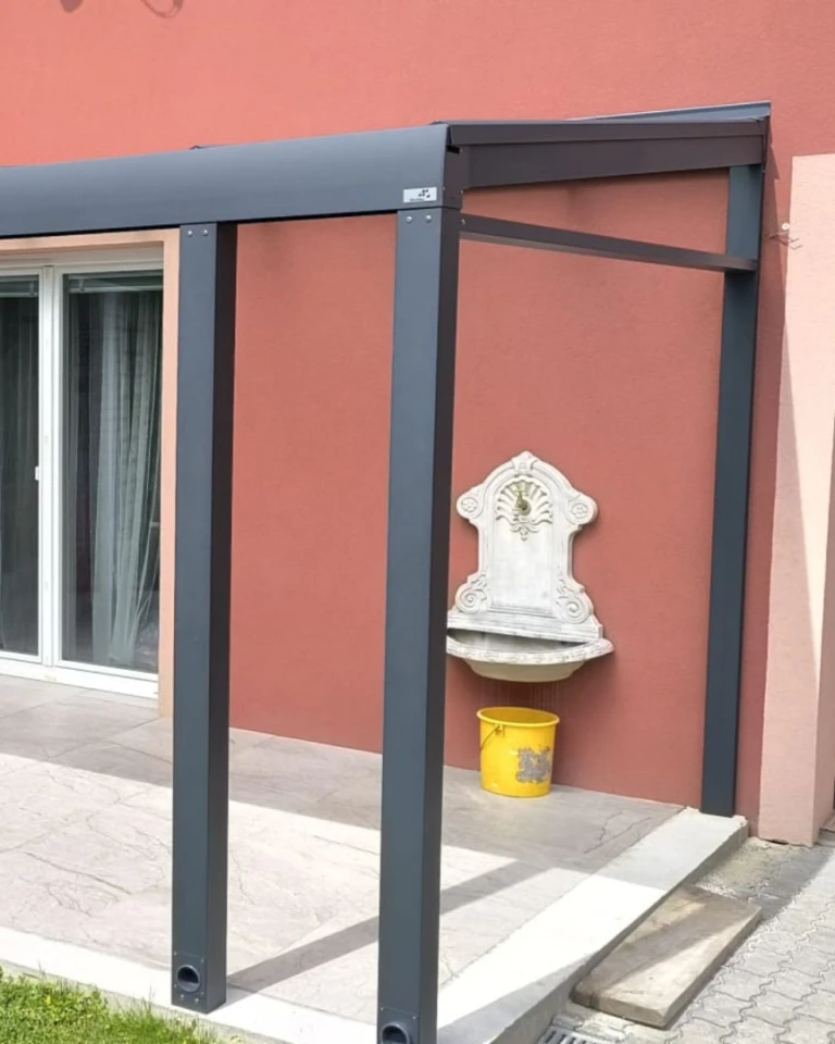 Vue détaillée de la structure porteuse et de la fixation de la pergola en aluminium à la façade de la maison, avec un lavabo décoratif.