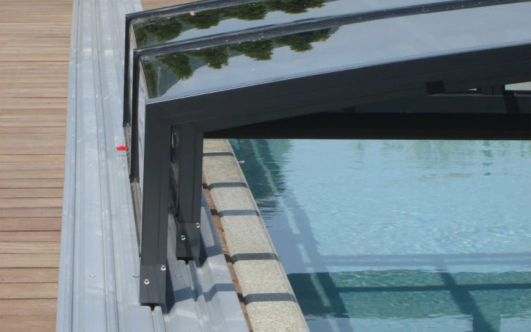 Vue détaillée de la structure en aluminium et des rails de l'abri de piscine sur la terrasse en bois.