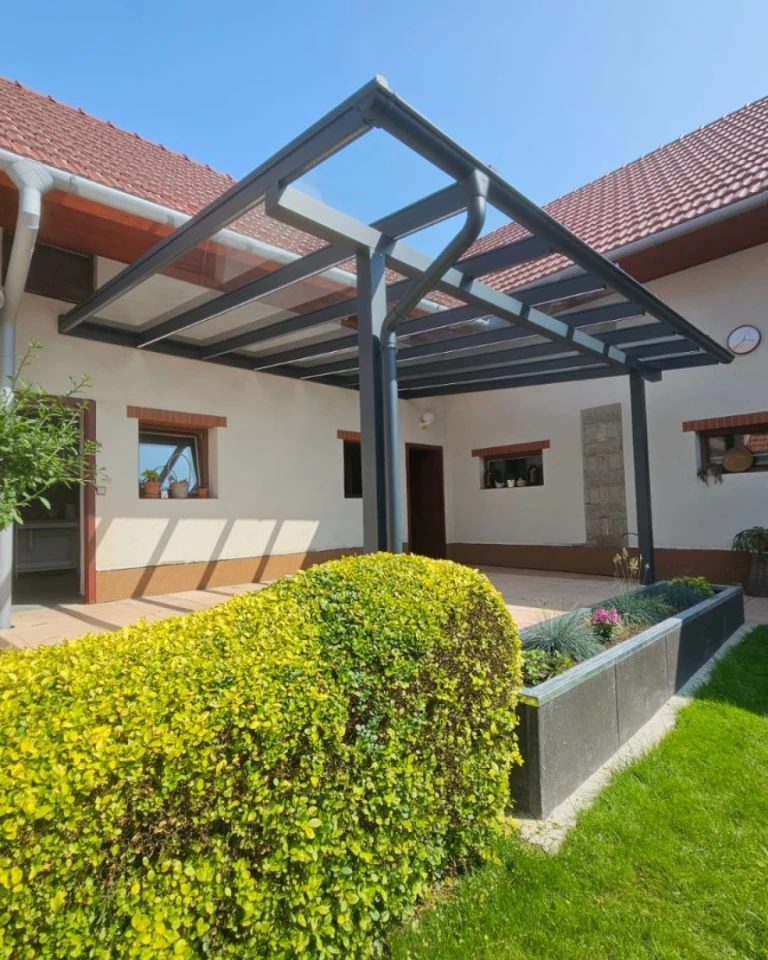 Une pergola moderne en aluminium avec un toit en verre, attenante à une maison individuelle dotée d'un jardin aménagé.