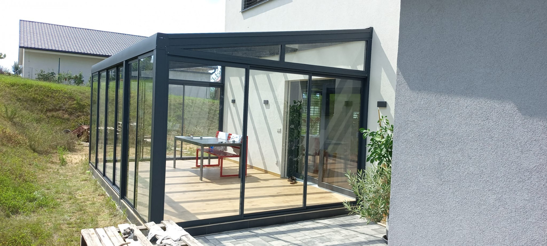 Une véranda moderne vitrée, dotée d'une structure anthracite et de portes coulissantes, attenante à une maison individuelle