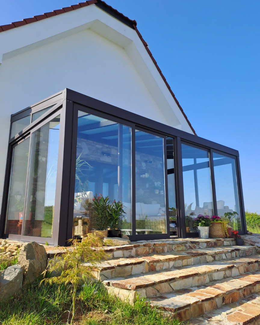 Une extension moderne vitrée attenante à une maison individuelle, avec un escalier en pierre et des fleurs.