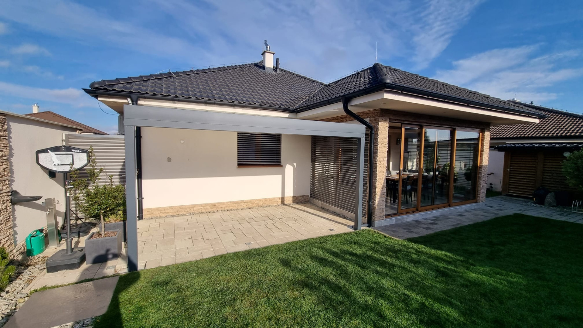 Une pergola moderne en aluminium gris près du bungalow, sur la terrasse pavée jouxtant le jardin