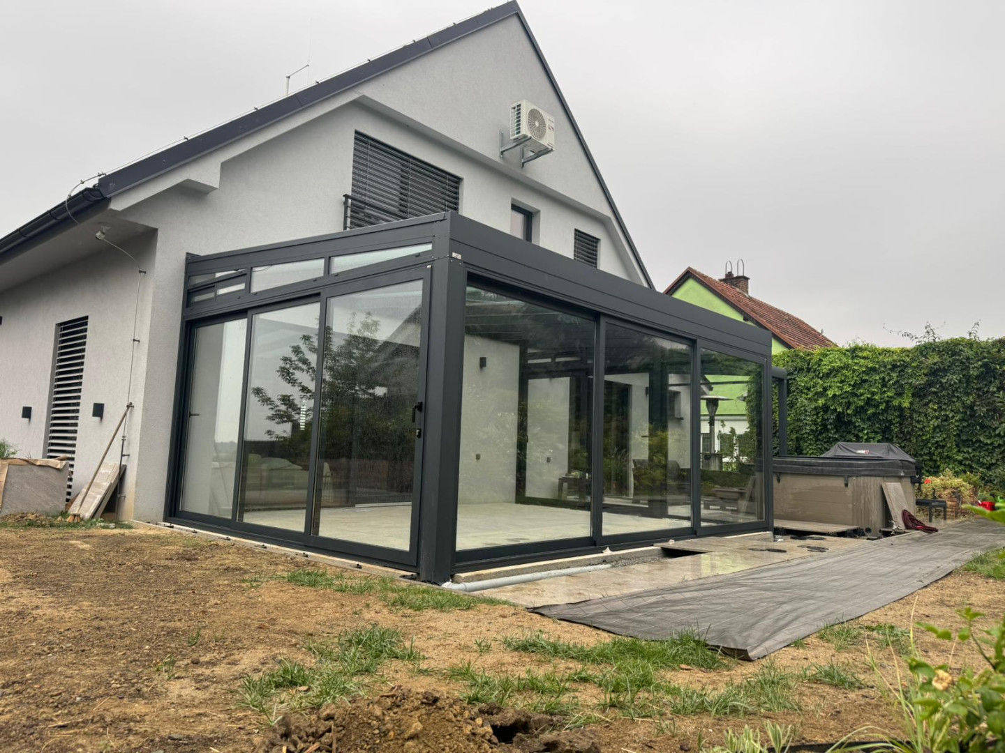 Une structure vitrée moderne, attenante à une maison individuelle, dotée d'un cadre foncé et de portes coulissantes.