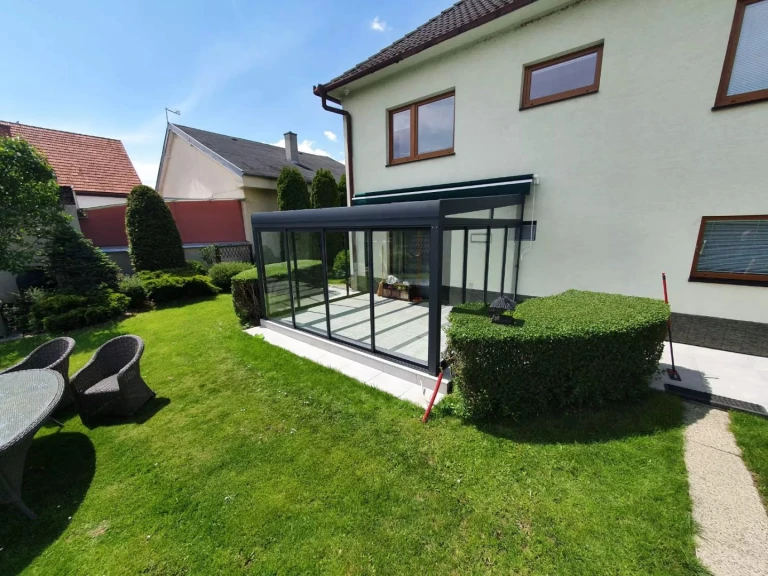Une véranda moderne vitrée, dotée d'une structure anthracite, adossée à une maison individuelle avec jardin.