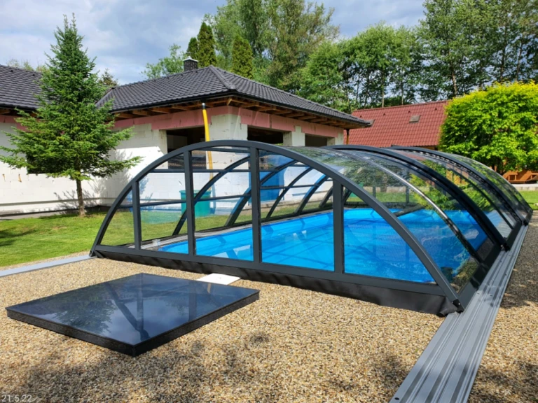 Une verrière en arc de couleur anthracite, avec un remplissage en verre, au-dessus de la piscine dans le jardin d'une maison individuelle.