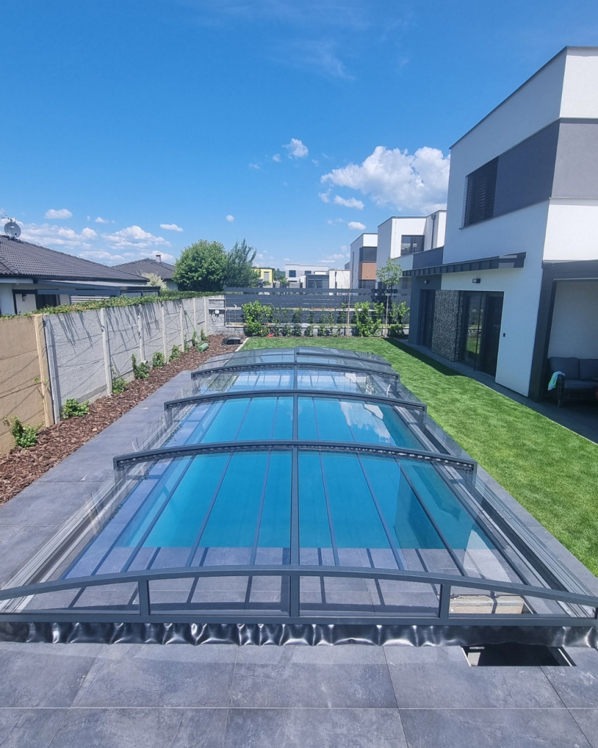 Une couverture de piscine moderne et basse, de couleur anthracite, dans un jardin familial avec pelouse