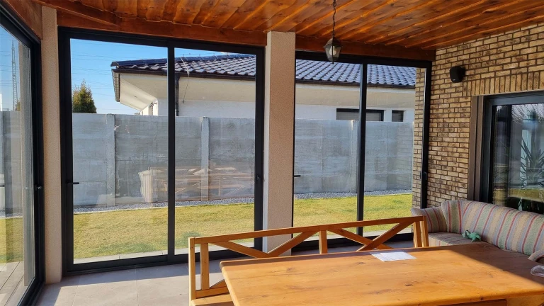 Vue de l'intérieur sur la baie vitrée en aluminium de la terrasse, avec ses portes coulissantes et sa vue sur le jardin