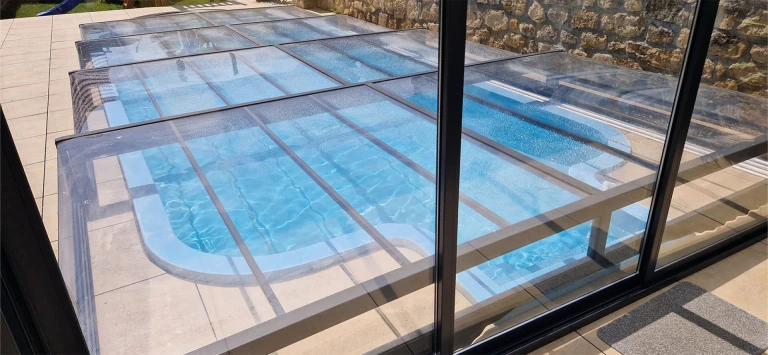 Vue de la couverture en aluminium fermée de la piscine EXCLUSIVE, avec un panneau transparent au-dessus de l'eau bleue