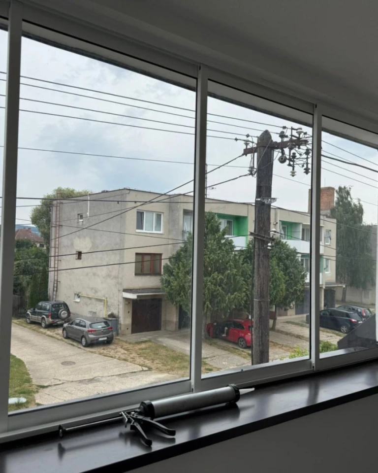 Vue à travers la nouvelle vitre sur la rue bordée d'immeubles d'habitation et de voitures ; un pistolet à encre est posé sur le rebord de la fenêtre