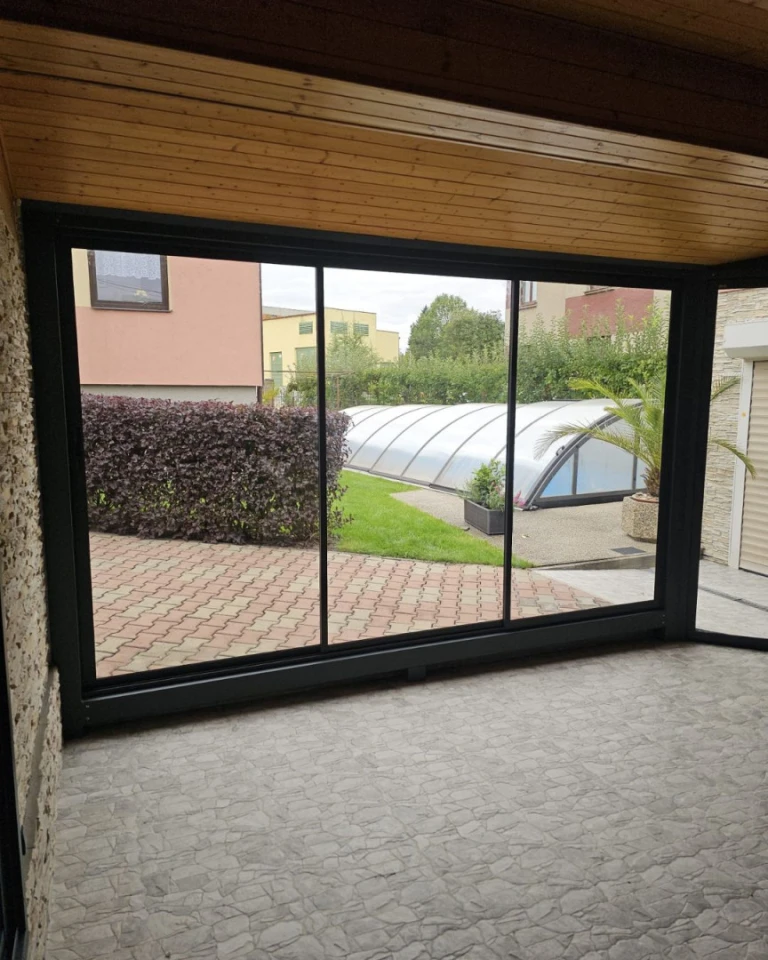 Vue depuis l'intérieur sur la terrasse vitrée aux cadres noirs, donnant sur le jardin et la piscine