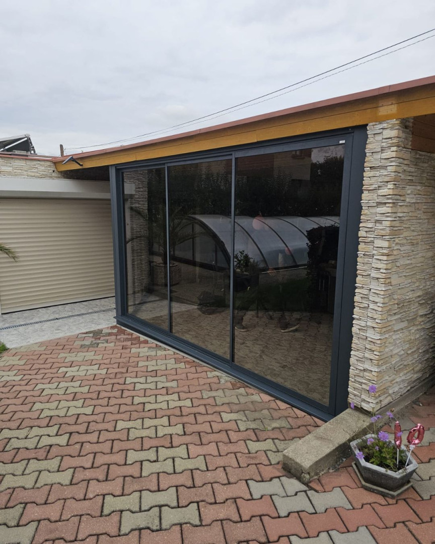 Portes coulissantes vitrées modernes donnant sur la terrasse, avec un cadre anthracite et un revêtement en pierre.