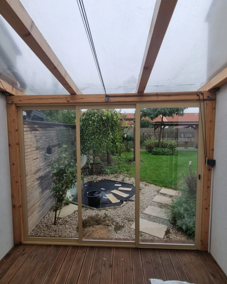 Vue depuis l'intérieur sur la terrasse vitrée à ossature bois, donnant sur le jardin