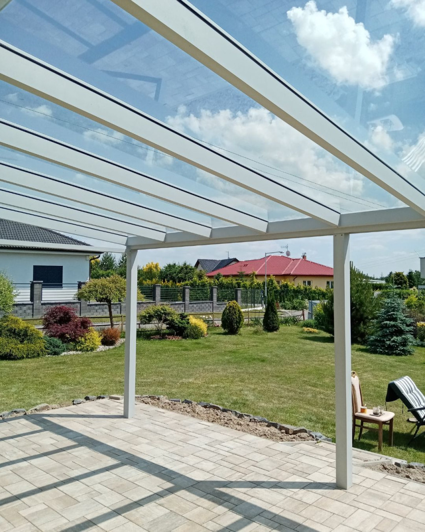 Vue depuis sous une pergola en aluminium vitrée sur un jardin bien entretenu avec une pelouse et des maisons individuelles en arrière-plan.