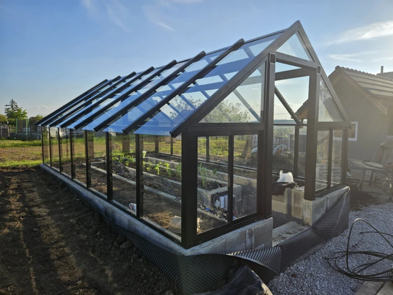 Une serre moderne vitrée, dotée d'une structure en aluminium noir reposant sur des fondations en béton, dans le jardin