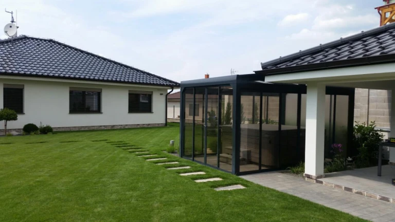 Un abri moderne vitré avec un jacuzzi, situé dans le jardin aménagé d'une maison individuelle.