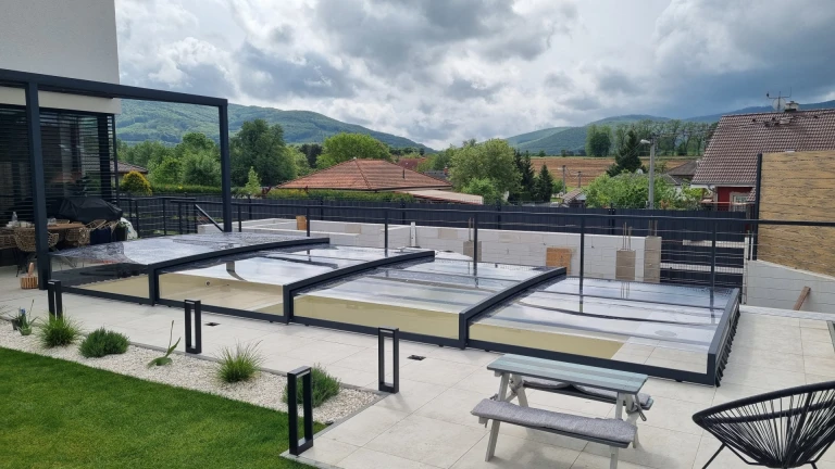 Abri de piscine moderne et bas EXCLUSIVE, avec une structure anthracite, installé sur la terrasse d'une maison individuelle