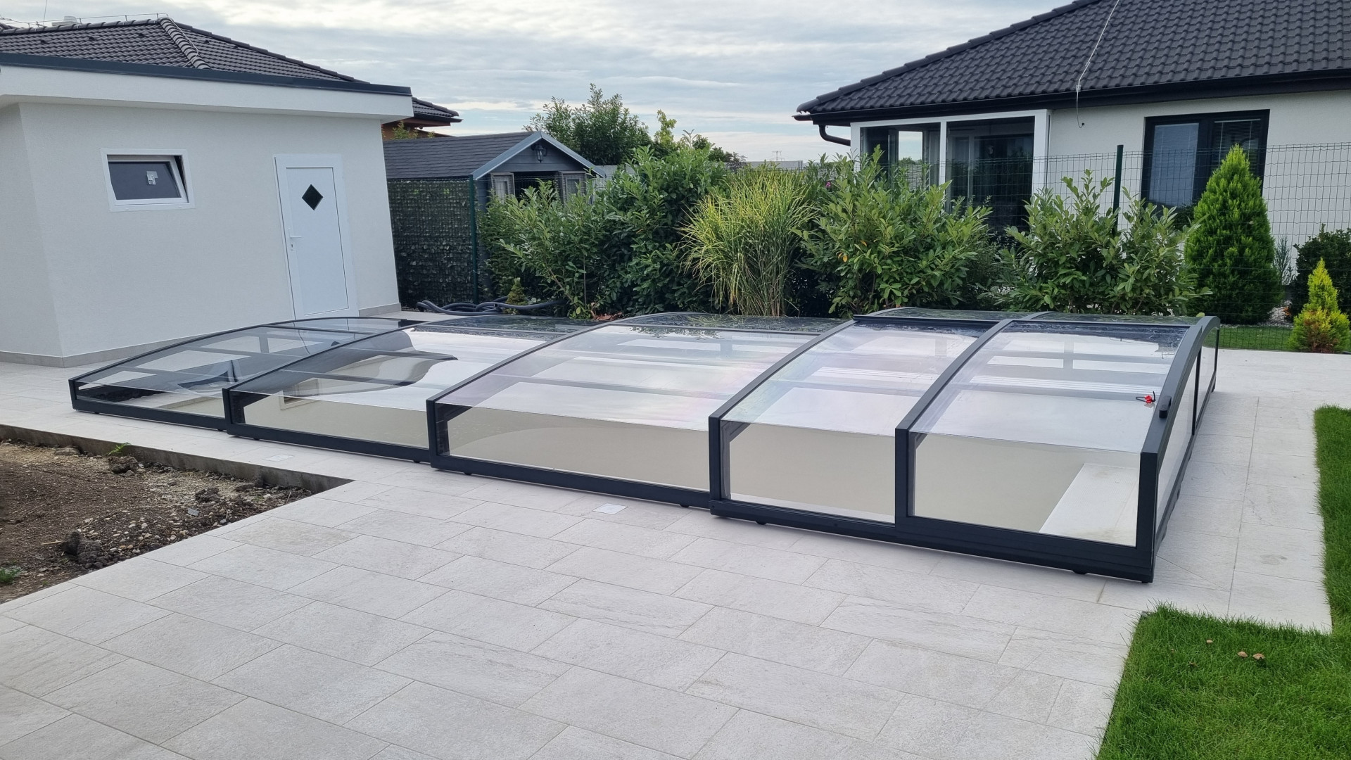 Une couverture de piscine moderne et basse, dotée de profilés noirs, sur la terrasse d'une maison individuelle