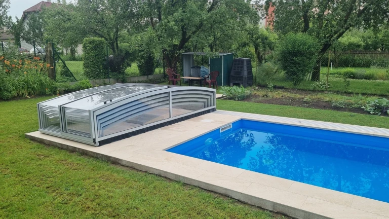 Une abri de piscine moderne et bas, doté d'un revêtement transparent, à côté d'une piscine à ciel ouvert dans le jardin.