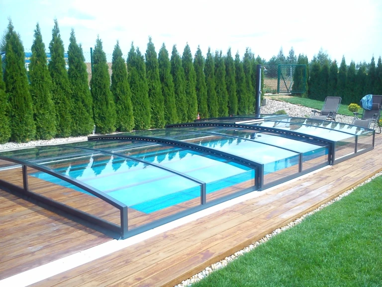 Une couverture de piscine moderne et basse, dotée d'un revêtement transparent, sur une terrasse en bois entourée de verdure