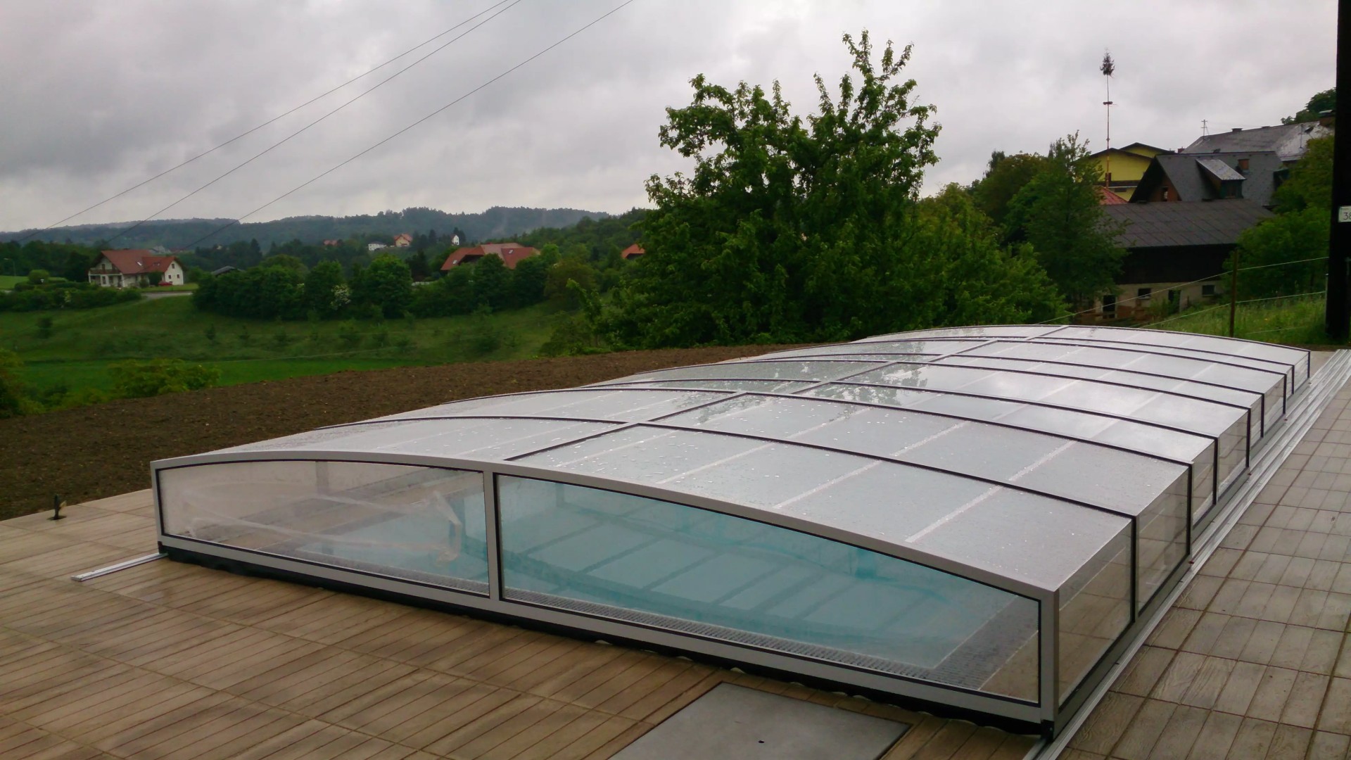 Une couverture de piscine moderne et basse de type STAR sur une terrasse offrant une vue sur un paysage vallonné et des maisons.