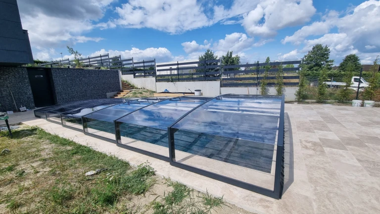Une couverture de piscine moderne et basse, dotée d'un cadre foncé et d'un vitrage transparent, installée sur la terrasse d'une maison familiale.