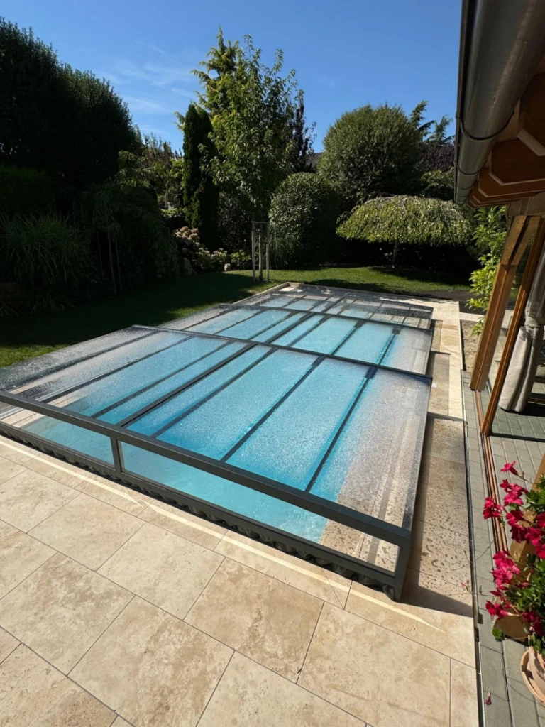 Une couverture de piscine moderne et basse, avec un cadre foncé et un panneau transparent, dans le jardin