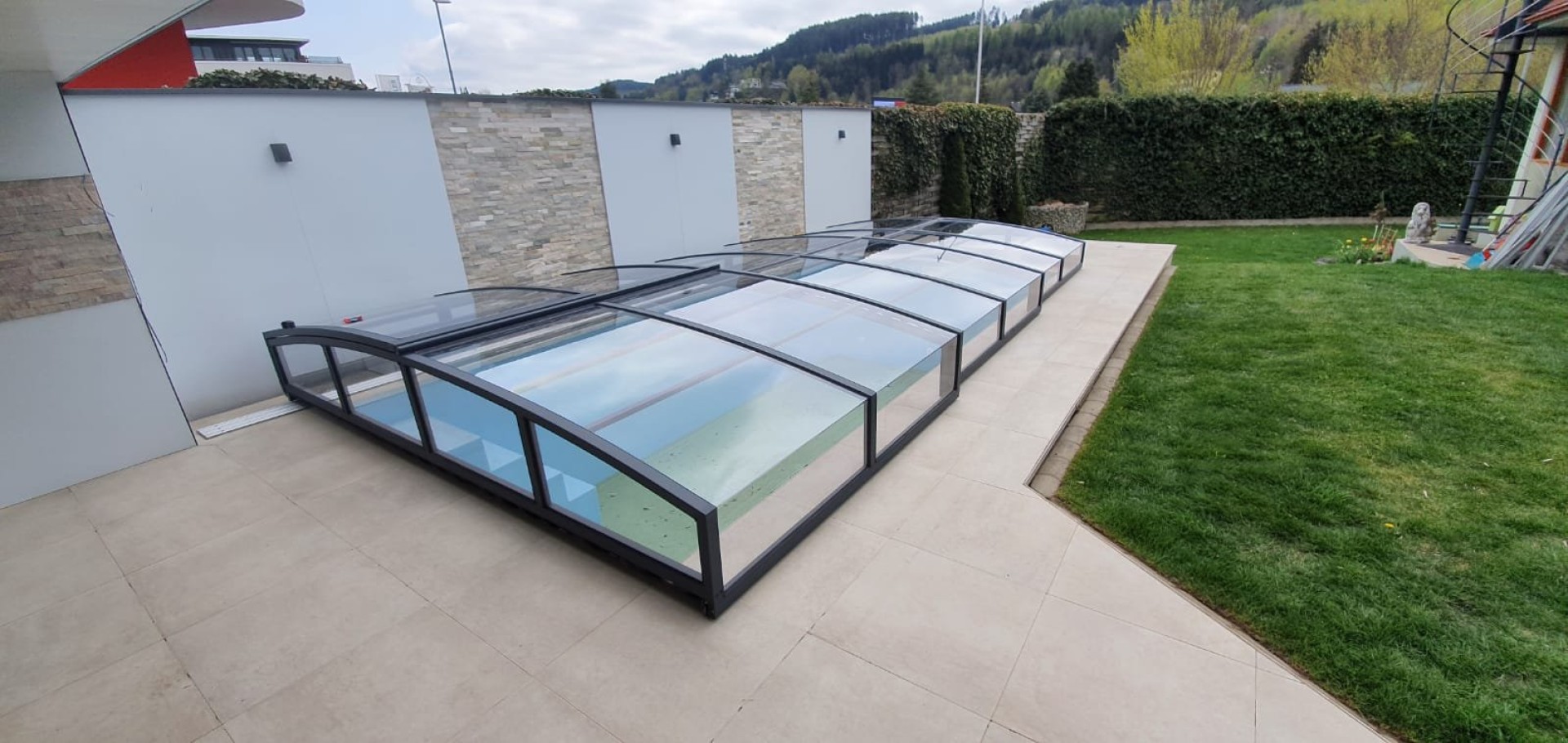 Une couverture de piscine moderne et basse, avec un cadre anthracite, installée sur la terrasse près du jardin
