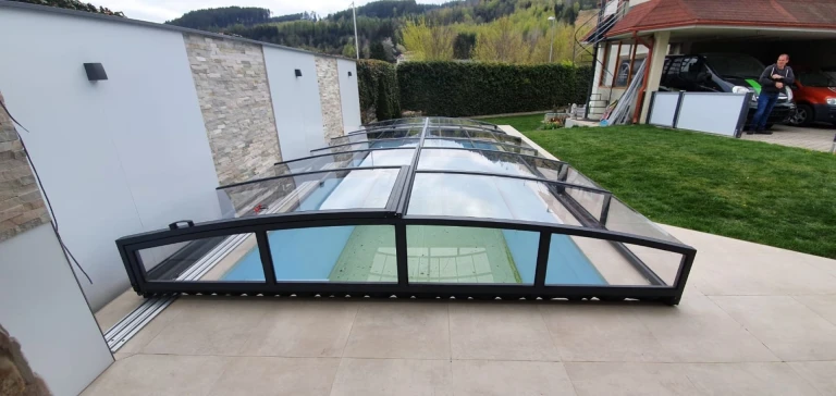 Un abri de piscine moderne et bas, avec une structure noire et des panneaux vitrés, dans le jardin