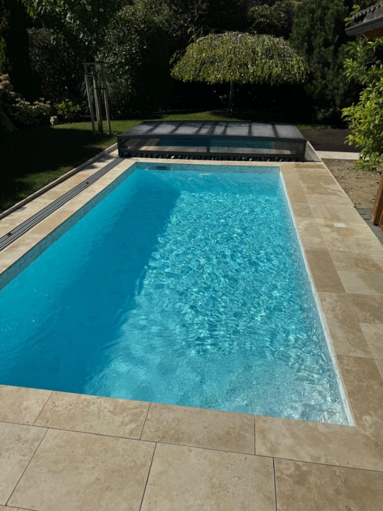 Une piscine moderne aux eaux cristallines, surmontée d'un auvent bas rétractable, dans le jardin
