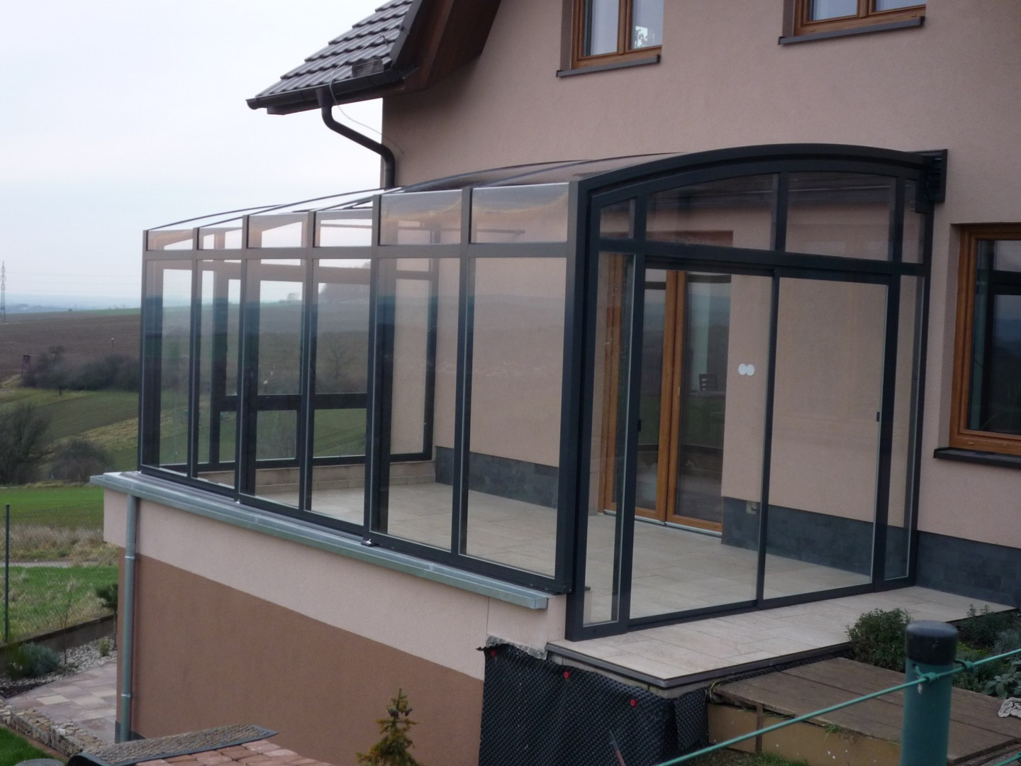 Une véranda coulissante moderne, dotée d'une structure en aluminium anthracite et d'un vitrage, aménagée sur la terrasse d'une maison individuelle.