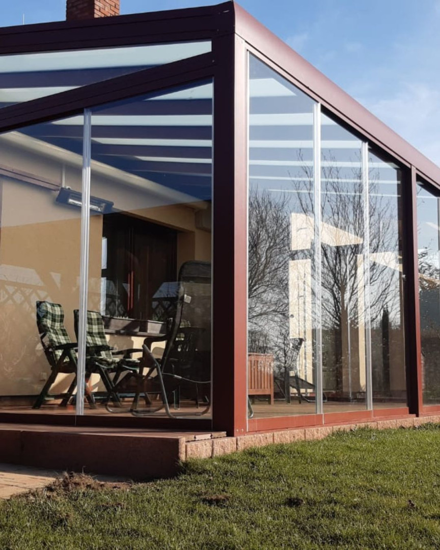 Une véranda moderne vitrée, dotée d'une structure marron et d'un coin salon extérieur sur la terrasse.
