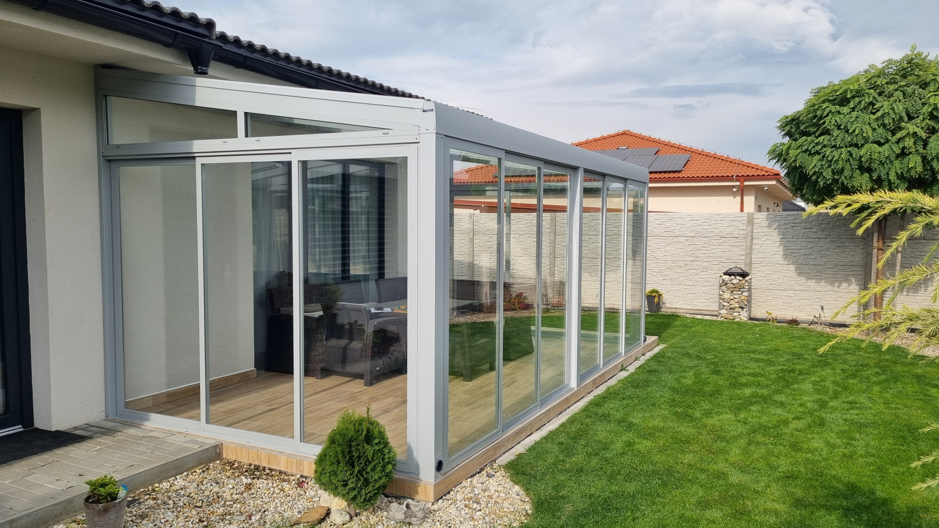 Une véranda moderne vitrée, dotée d'une structure en aluminium, attenante à une maison individuelle avec jardin